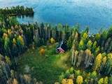 Luftfoto af en rød bjælkehytte med sauna i forårsskoven ved en sø i Finland