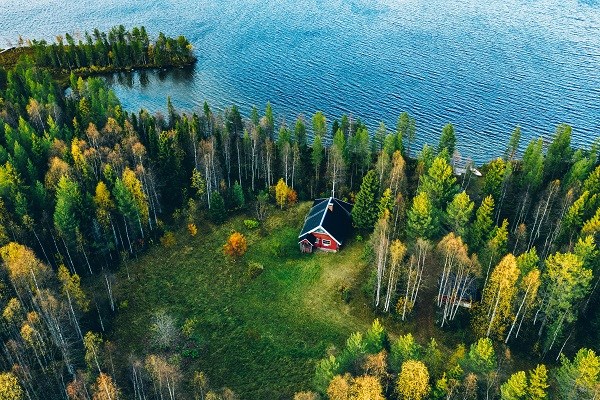 Luftfoto af en rød bjælkehytte med sauna i forårsskoven ved en sø i Finland